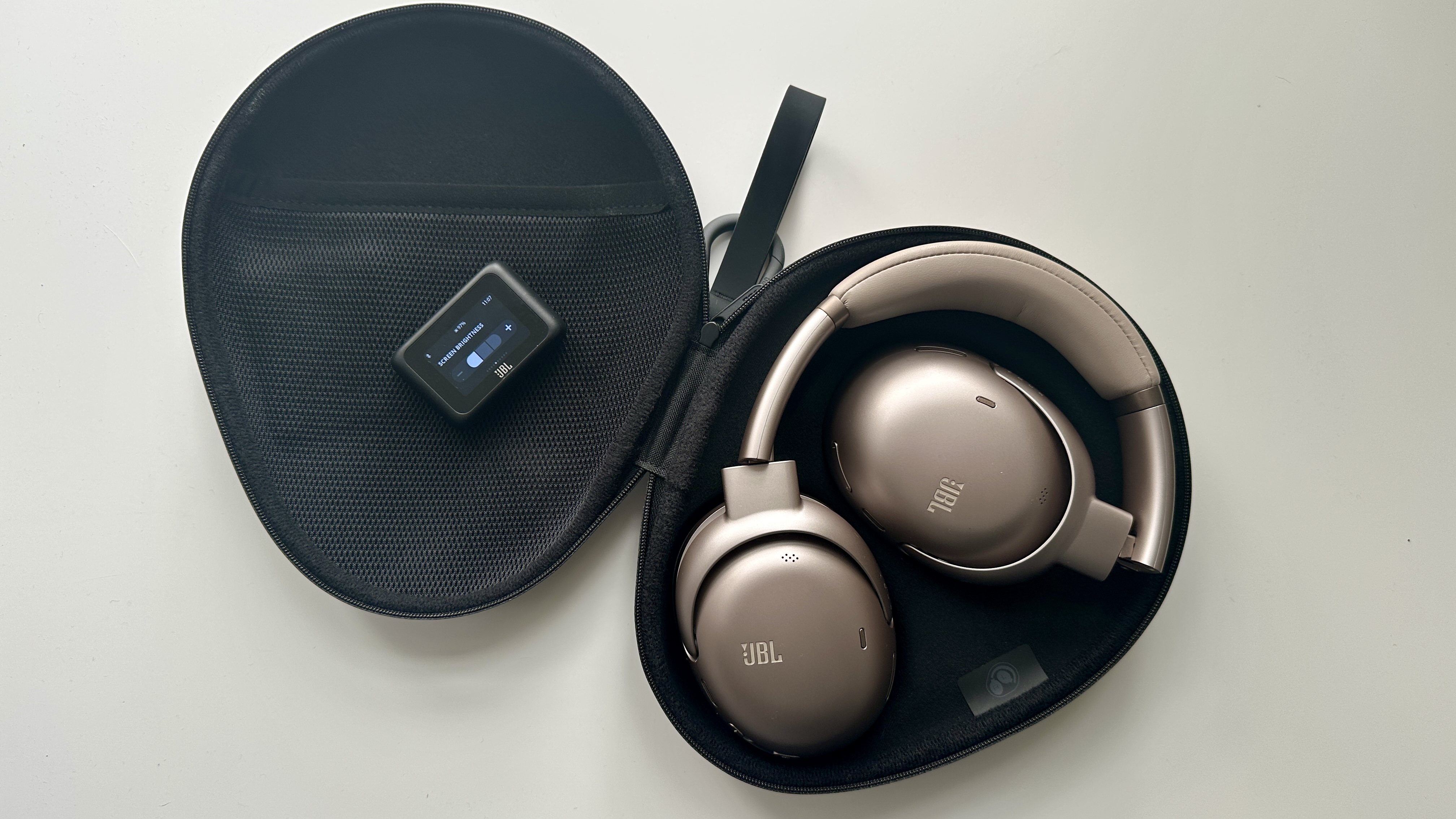 JBL Tour One M3 over-ear wireless headphones folded away in their carry-case, on a white surface