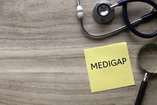 Top view of stethoscope, magnifying glass and yellow paper note written with Medigap on wooden background with copy space