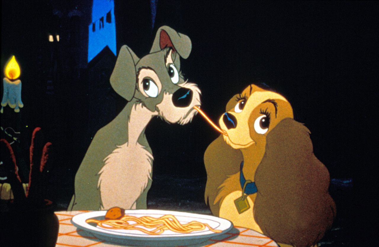 Animated still from Lady and the Tramp showing Lady and Tramp sharing a strand of spaghetti by candlelight.