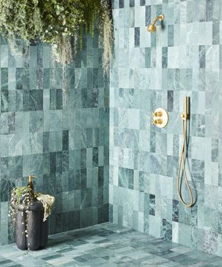 A walk-in shower with emerald marble tiled walls and flooring and brass fittings