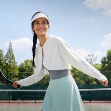 Woman playing tennis in white cap and light blue skirt