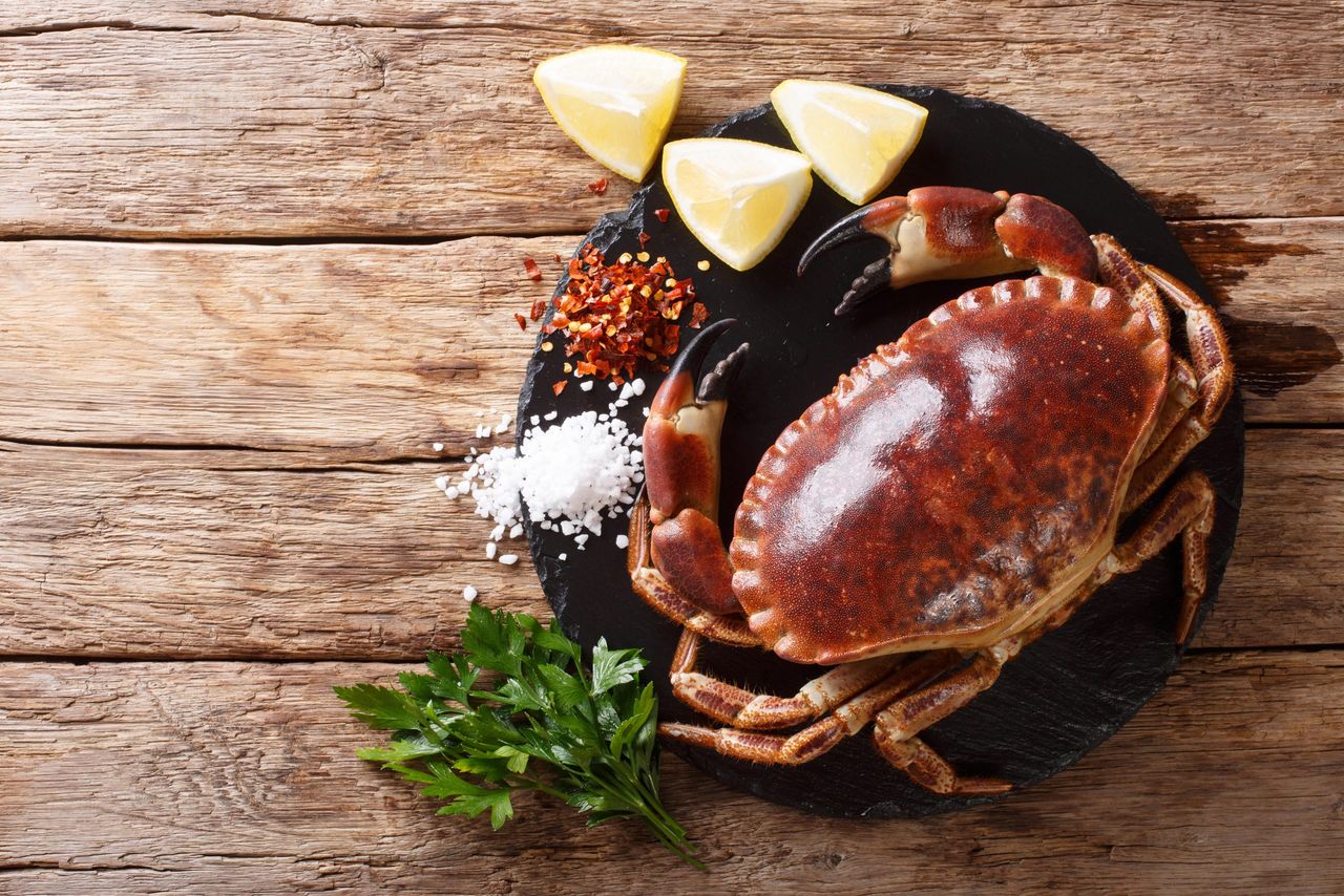 Raw brown crab with lemon, parsley and spices on a slate board close-up on a wooden table. horizontal top view from above