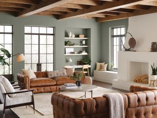 A living room with sage green walls, leather Chesterfield style sofas, and wooden beams on the ceiling