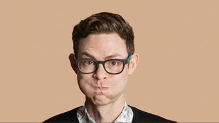 Man wearing glasses blowing his cheeks out against beige background