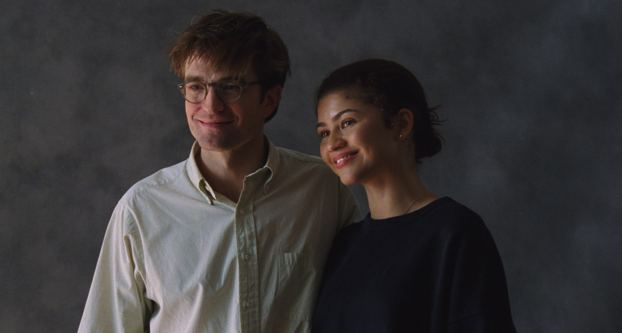 robert pattinson and zendaya as charlie and emma trying to smile and pose for wedding photos in a photo studio in a still from the movie the drama