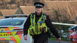 Catherine Cawood played by SARAH LANCASHIRE wearing police uniform and walking away from a police crime scene in Happy Valley season 3