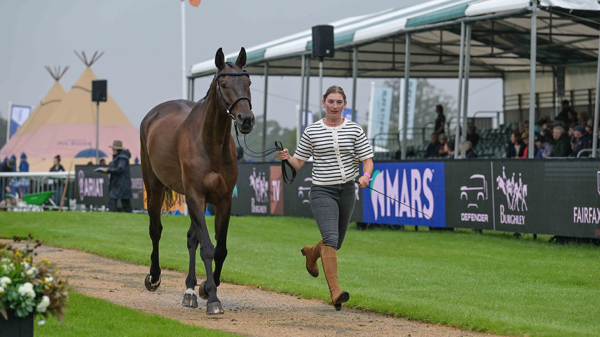 Nadja Minder, a rider in jeans, long brown boots and a stripey top, trots up Toblerone, a bay horse at the Burghley Horse Trials first trot-up 2026