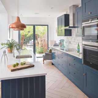 Kitchen in side return extension with dark blue units and light worktops and copper pendant over island