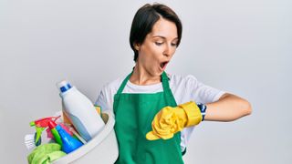A woman holding cleaning equipment while looking at her watch