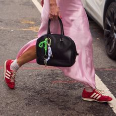a woman wearing a pink silk dress wearing red sneakers carring a black handbag