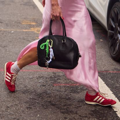 a woman wearing a pink silk dress wearing red sneakers carring a black handbag