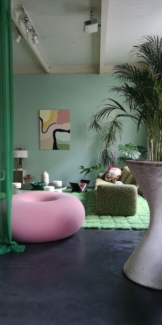 A living room with deep green walls and a bright pink ottoman