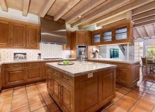 A kitchen with wooden cabinets, a large wooden island in the centre, and red terracotta floor tiles