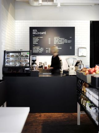 Black deli counter with a female staff member and the menu on the wall behind