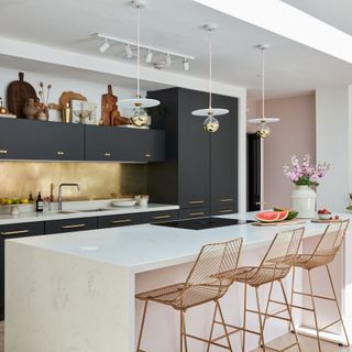 Kitchen area in open-plan space with dark units, white breakfast bar and gold splashback