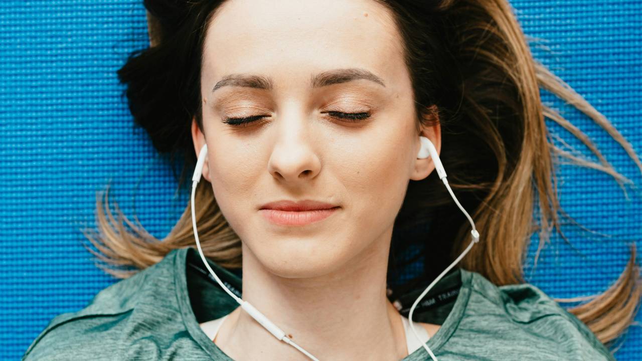 A woman asleep on a blue mat with wired earbuds in