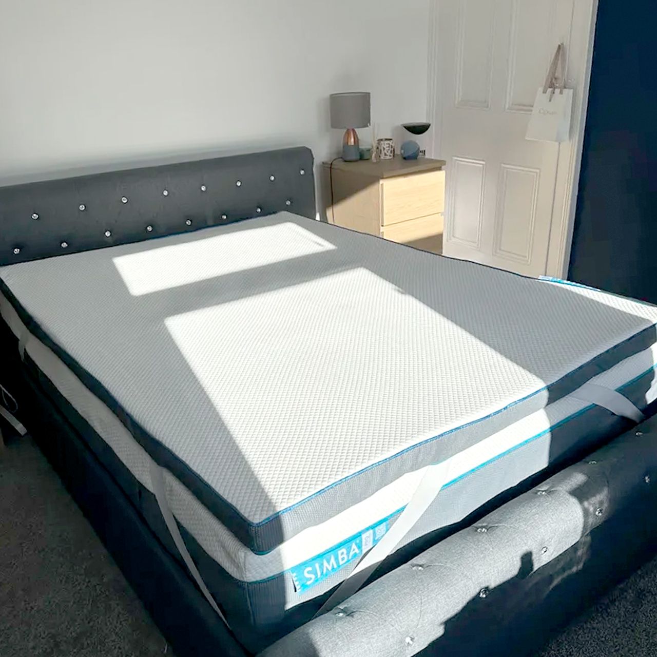 The Simba Hybrid mattress topper being tested in a bedroom with a grey upholstered double bed