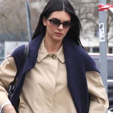 Kendall Jenner seen out in Milan during Milan Fashion Week 2026. The supermodel stepped out in the city wearing a black The Row bag, a khaki trench coat, white pants, and black high-vamp pumps from Phoebe Philo.