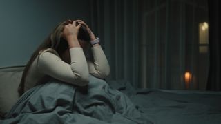 Woman sitting in bed clutching her head in frustration after waking up from a nightmare