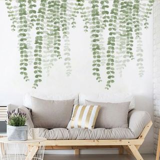 Green plant wallpaper with a wooden sofa topped with neutral colored cushions and a wooden top coffee table accessorized with a plant