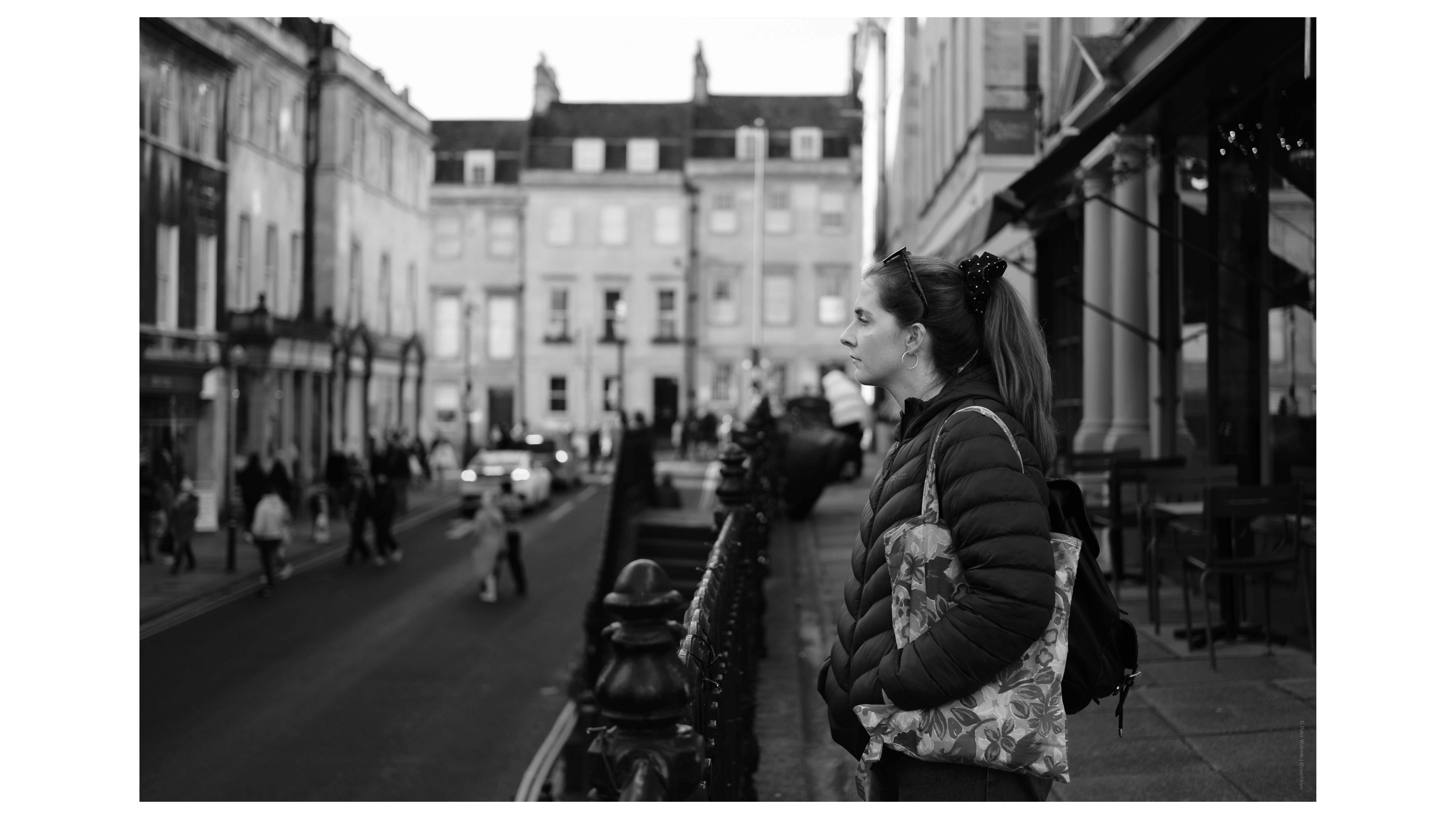 A black and white photo of a woman standing looking across a road