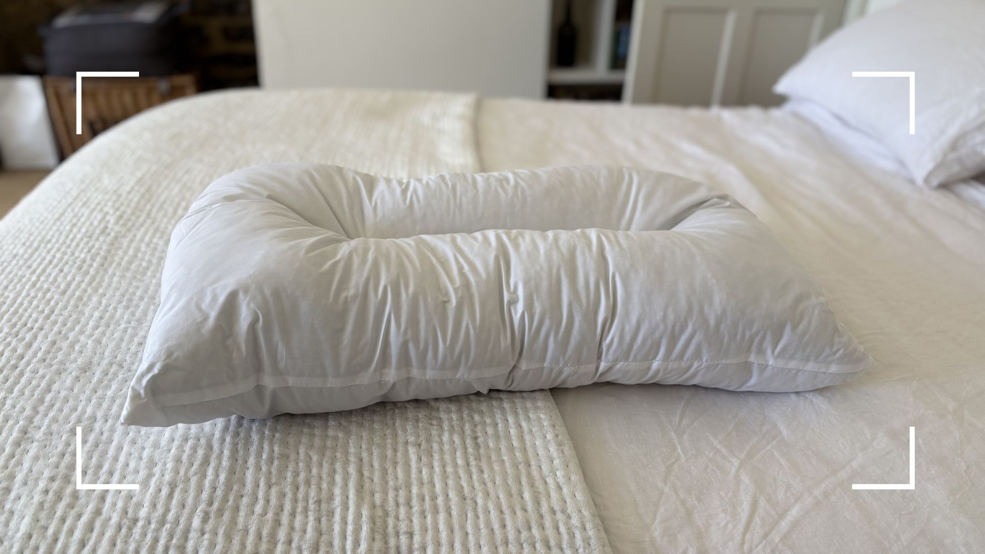 Naturalmat The Centre Stitched Wool Pillow on a bed, lying on its side to show off the shape
