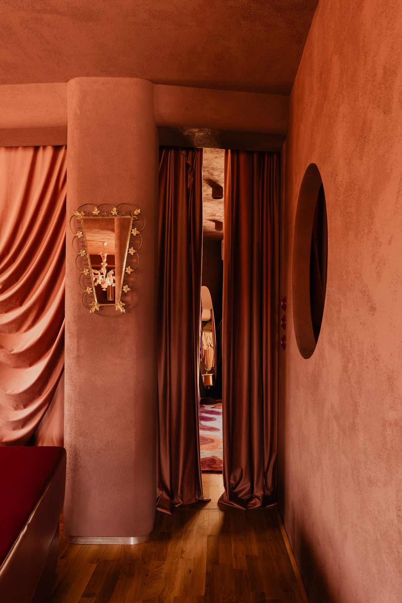 A mirror hangs on a textured wall opposite a wall with a porthole opening.