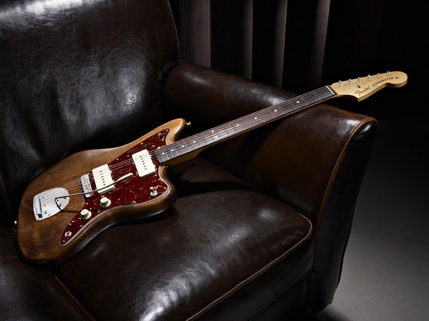 A lovely brown guitar lounges on a nice leather couch