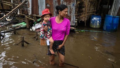 A woman carrying her child wades through flood water in Myanmar