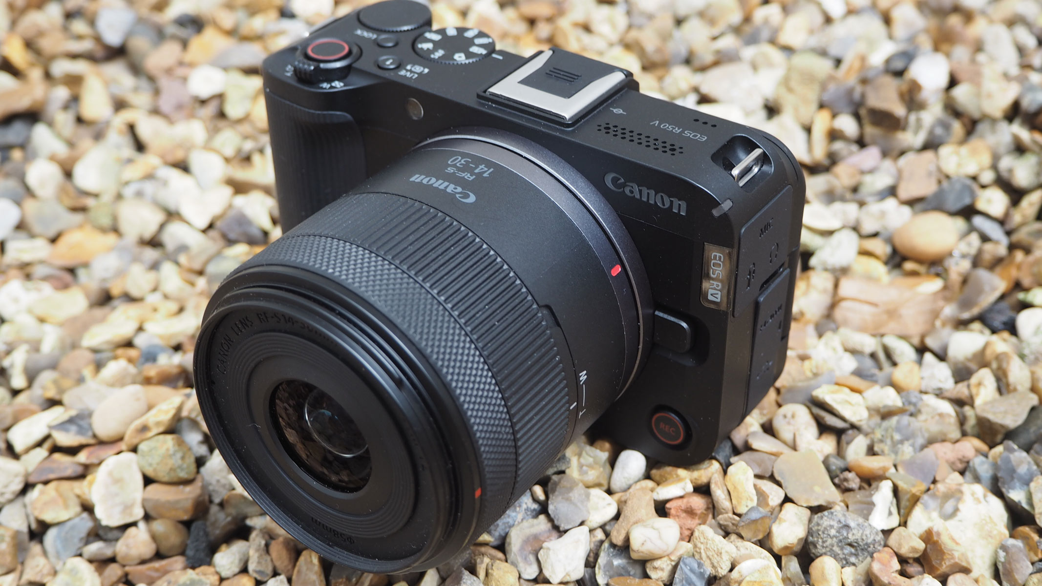 The Canon EOS R50 V on gravel, side view from the right side.