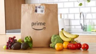 A brown Amazon Prime bag full of groceries in a kitchen. Next to the bag is a pile of fruit and vegetables