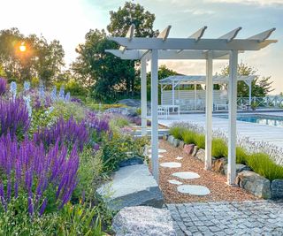 gravel path, stone edging, purple flowers and archway near pool in garden designed by Annika Zetterman