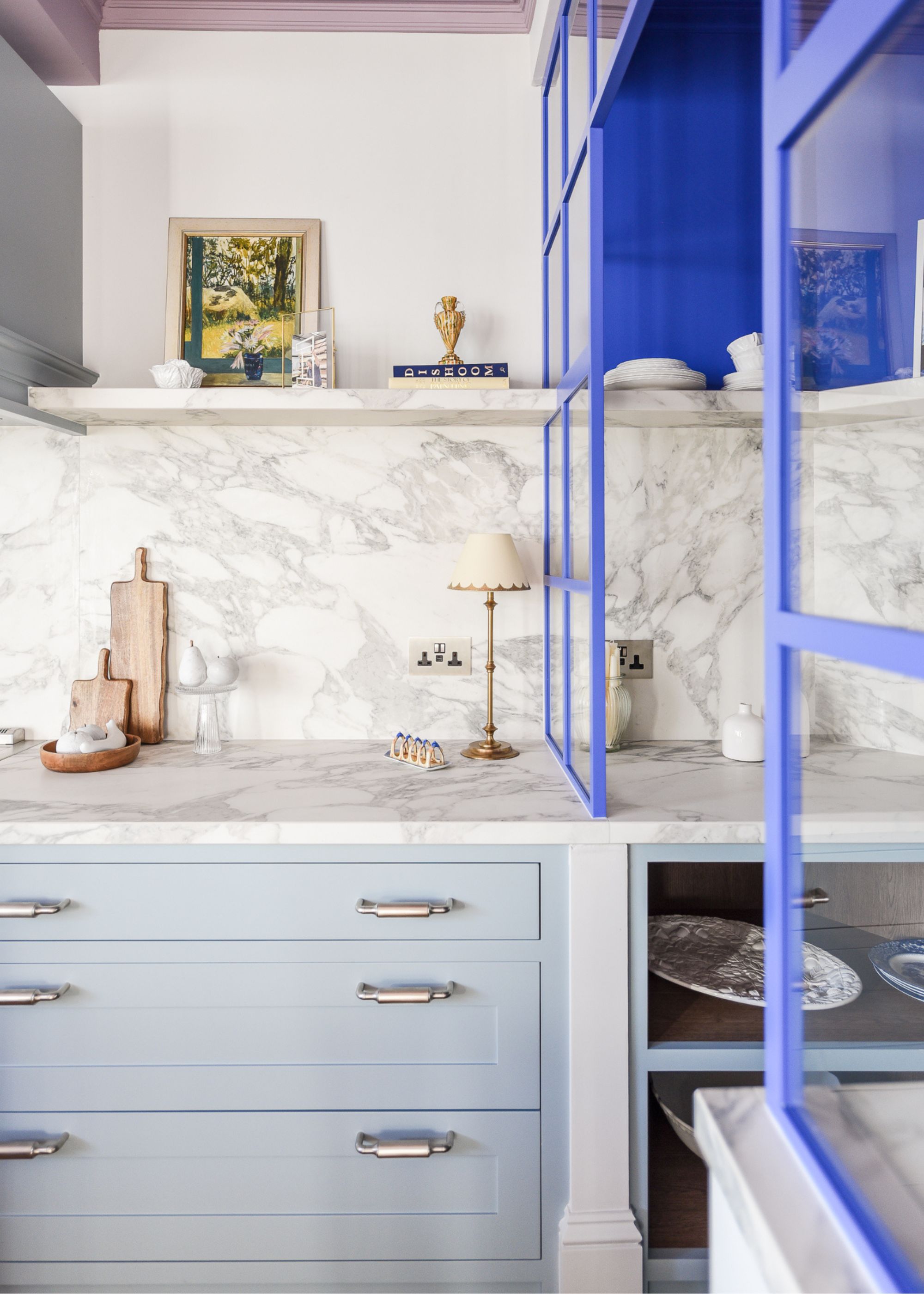 A baby blue kitchen with dark blue cabinets. There is veined marbled countertops that draws up to the splashback.