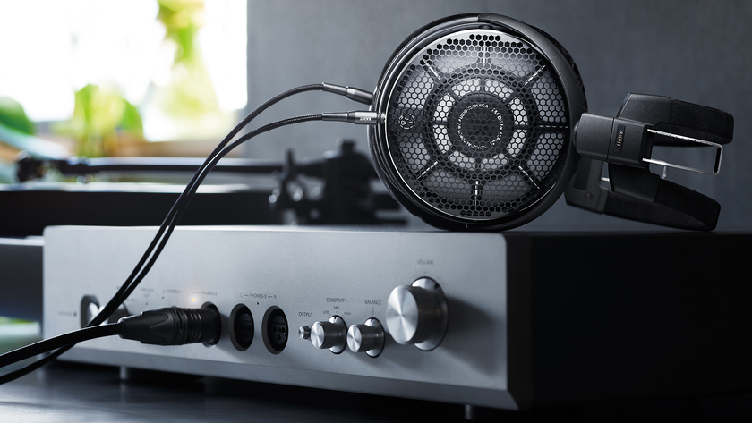 Product photography of the Audio-Technica ATH-ADX7000 over-ear headphones atop a headphone amp with a window in the background