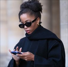 llie Delphine wears Celine sunglasses, a black oversized wool scarf, a black coat from Toteme, black cropped pants, during a street style fashion photo session, on November 06, 2023 in Paris, France. (Photo by Edward Berthelot/Getty Images)