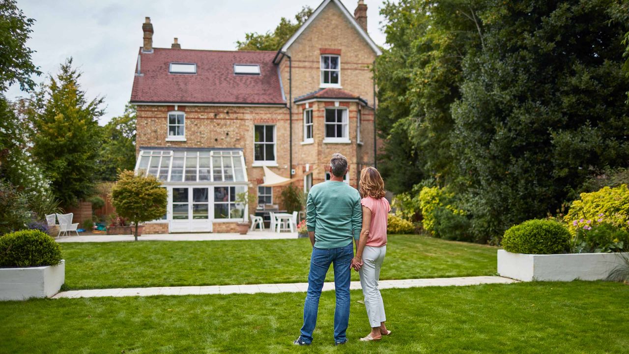 A couple look wistfully at a large brick home.