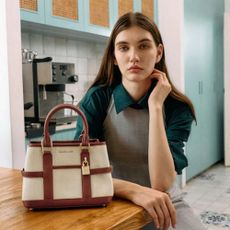 Young woman wearing Charles 
Keith clothing sat next to tan and white bag in kitchen