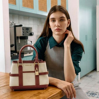 Young woman wearing Charles & Keith clothing sat next to tan and white bag in kitchen