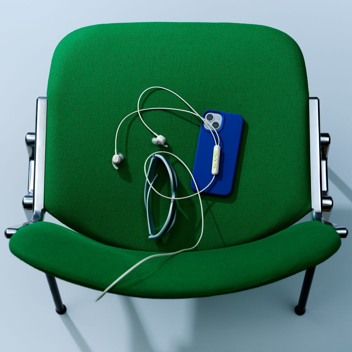 wired earphones with an iphone and sunglasses on a green chair