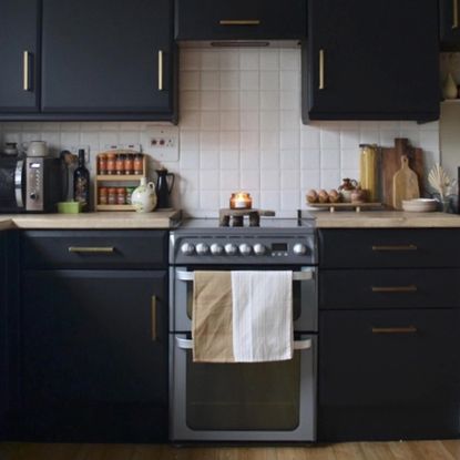 kitchen with dark painted cabinets, painted tiles and an oven with tea towel