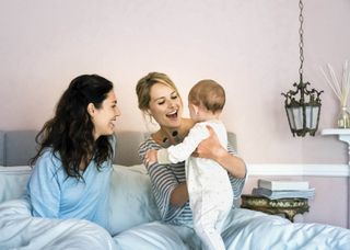 Happy young lesbians playing with baby boy in bed, by Portra