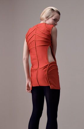 Young female model, back to the camera, wearing a red Odysee dress by Ara fashion, navy blue tights, pale grey background