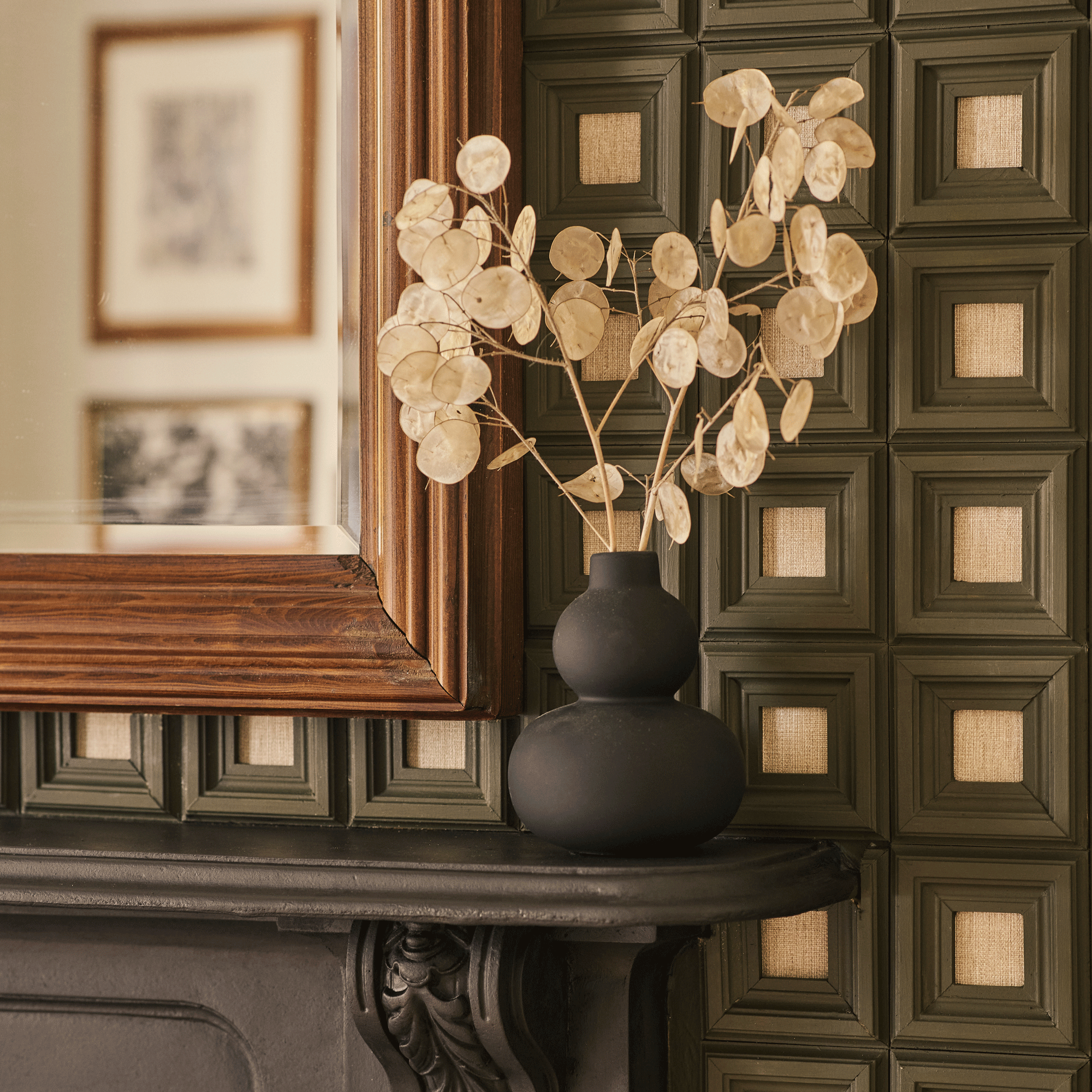 a close up of a living room mantelpiece with a black vase filled with dried Lunaria or honesty plant