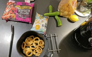Airfryer med forskjellige matvarer rundt seg på en kjøkkenbenk