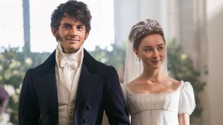 From left to right: Jonathan Bailey smiling as Anthony with Pheobe Dynevor standing alongside him as Daphne in a wedding dress.