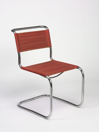 A cantilevered tubular metal chair by Marcel Breuer with red fabric seat and backrest