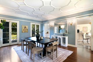 A modern dining room painted in a light blue with a black table and beige velvet chairs