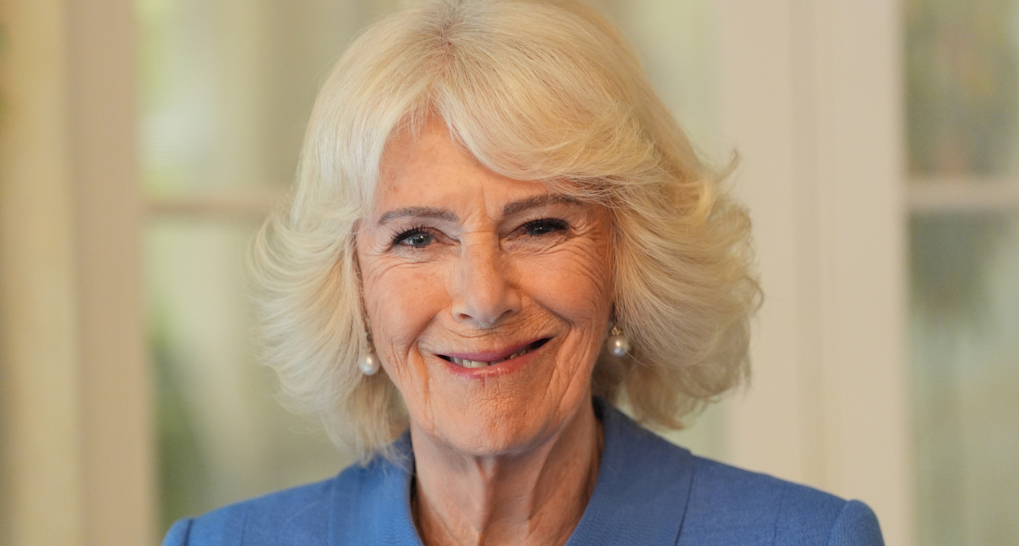 Queen Camilla wearing a blue coat and smiling