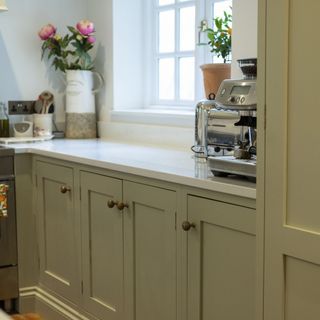 sage green kitchen cabinets, white kitchen worktop with coffee machine