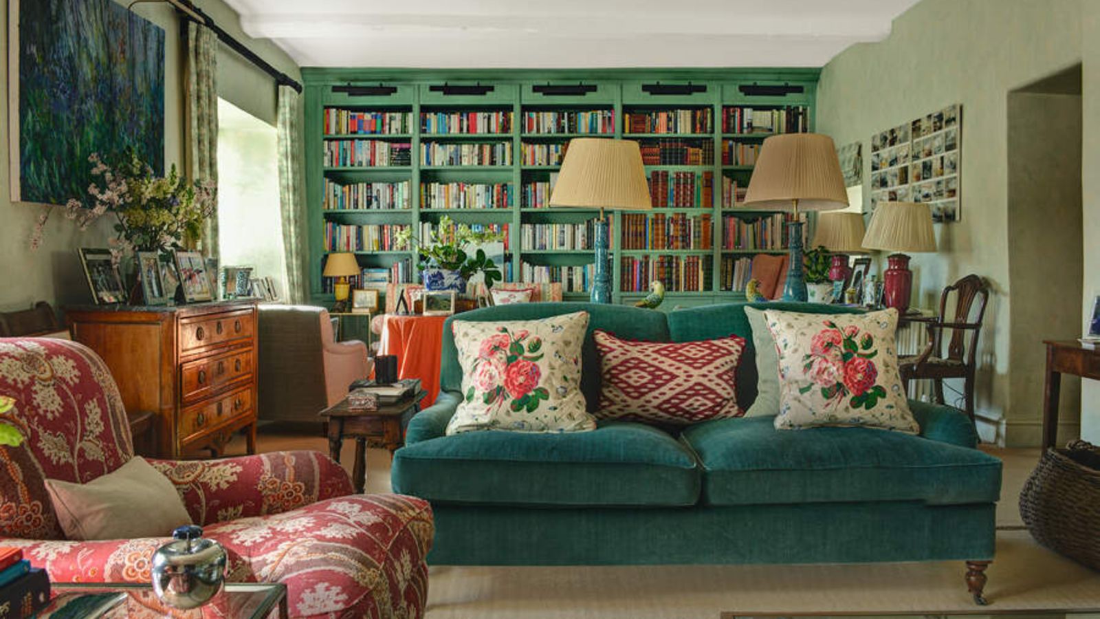 A country living room with a blue sofa and red patterned arm chair. Built in blue book cases line the back wall. 